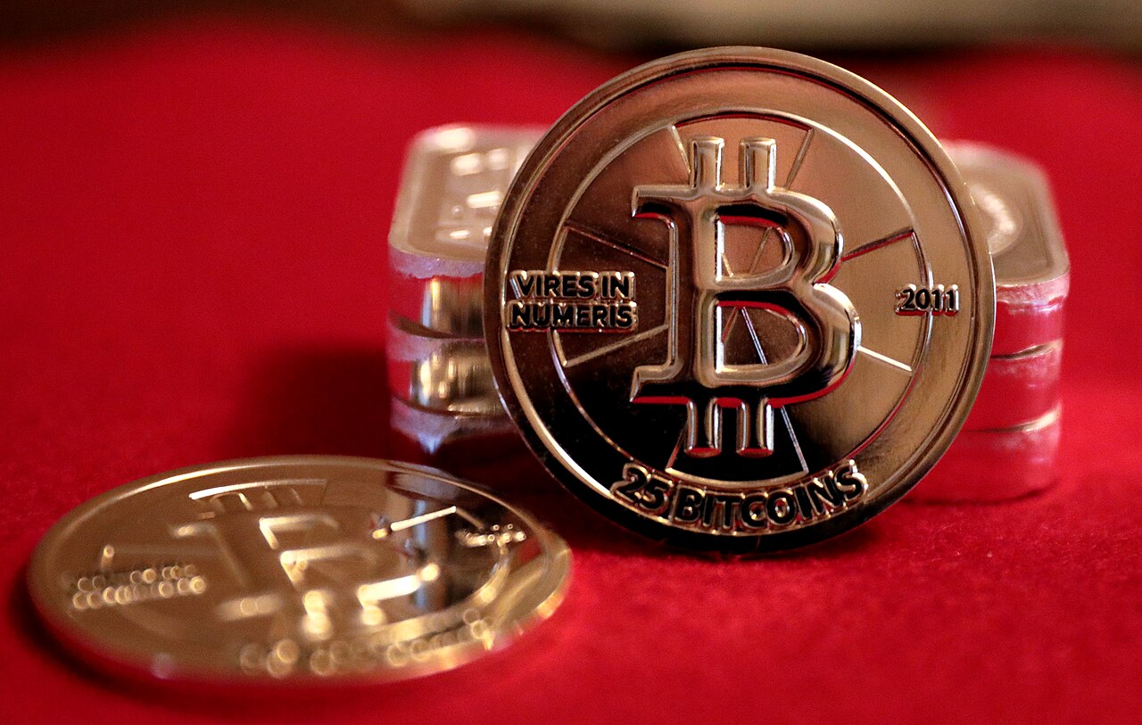 Two 2011 Casascius 25 Bitcoin gold-plated pieces on red fabric, showing the obverse and edge profile